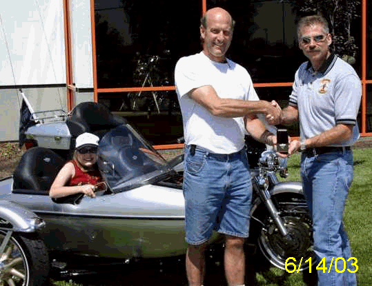 Jeff gets Gold Key to Legacy Ride Motorcycle from Mike Cornell as MDA Ambassador Lexi looks on in style